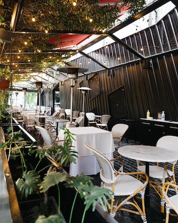 Vista de la terraza exterior del Nomad Restaurante con mesas de mármol y sillas de mimbre, rodeada de plantas, luces de guirnalda y estufas