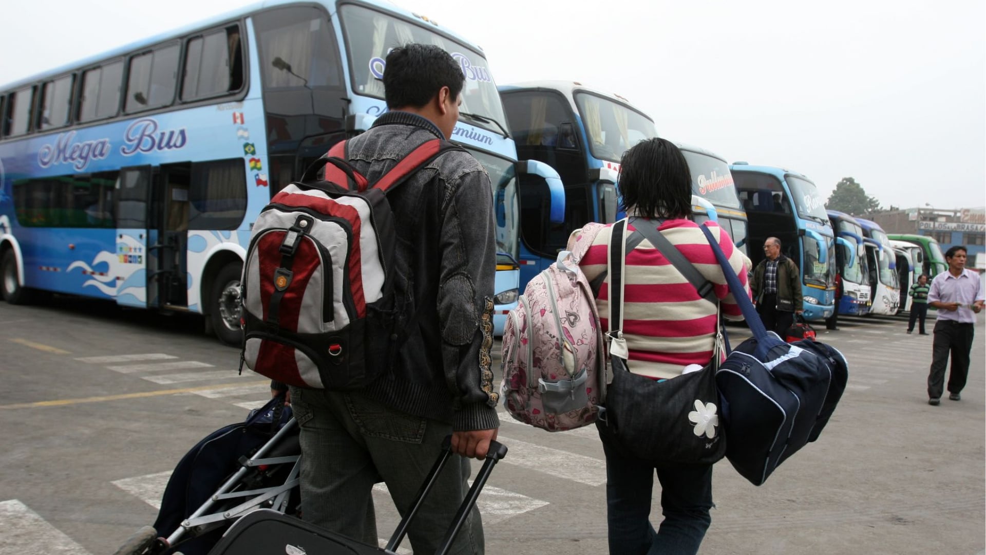Dos personas con equipaje caminan en un terminal de autobuses, un escenario habitual durante los feriados que impulsan el turismo interno en Perú.