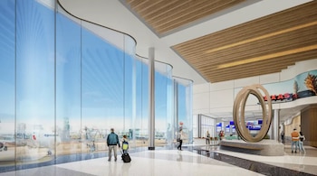 Interior de una terminal de aeropuerto moderna con ventanales grandes. Se ven pasajeros, una escultura y un avión de American Airlines en la pista exterior