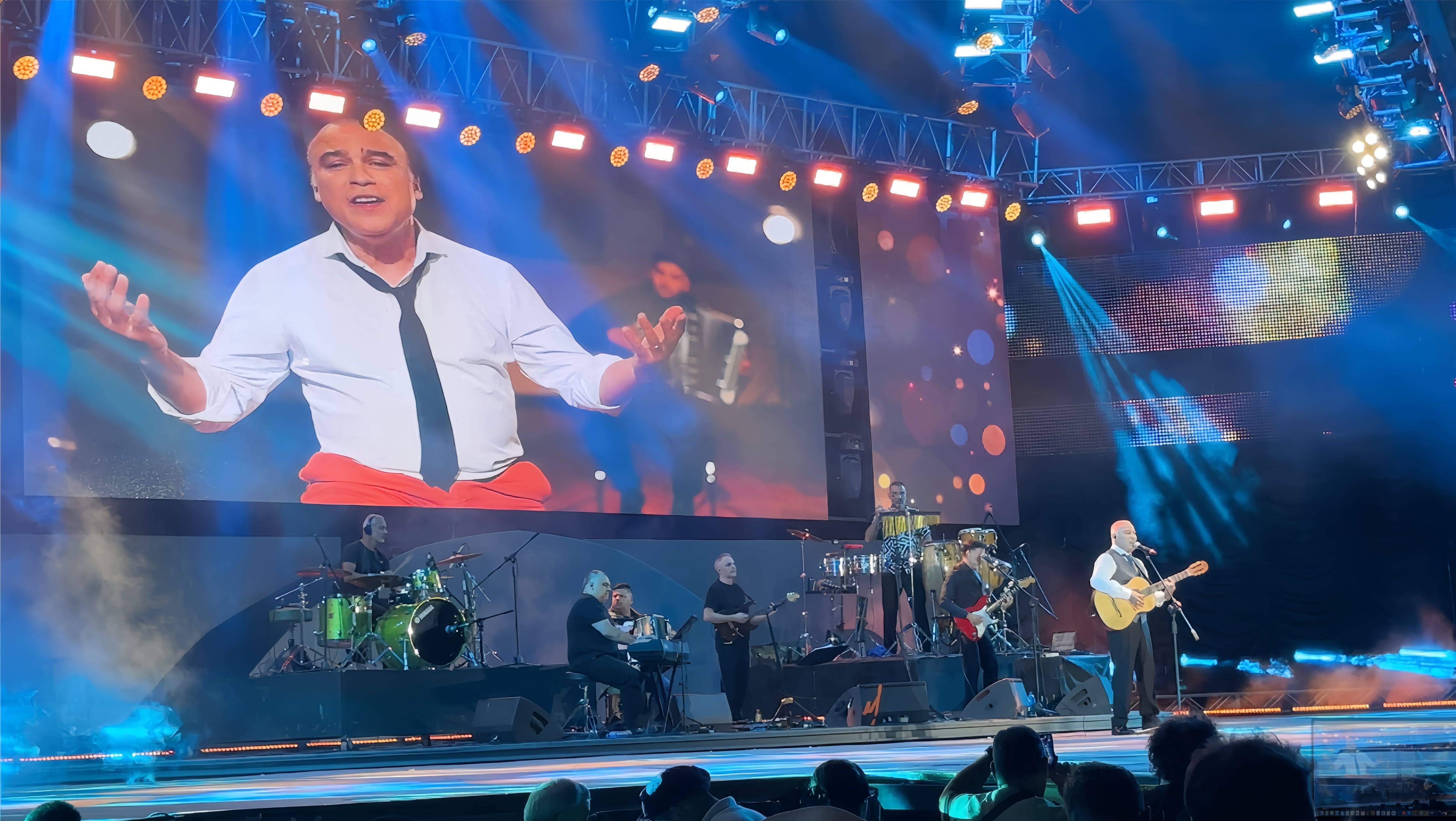 El reconocido cantante Paz Martínez ofrece una vibrante actuación en vivo en el festival de Cosquín, acompañado por su banda y con proyecciones visuales de fondo.