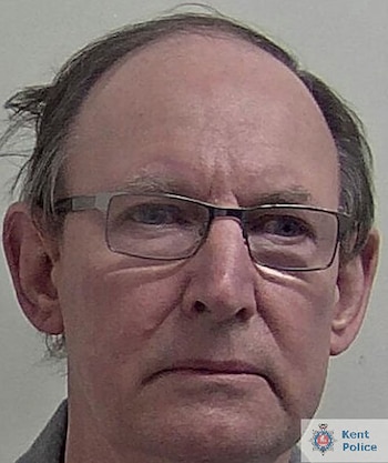 Primer plano del rostro de un hombre con cabello oscuro escaso y gafas. Fondo de color gris claro. Logo de la Policía de Kent en la parte inferior derecha
