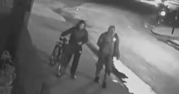 Una mujer joven con un vestido de lentejuelas negro, un collar de perlas, pendientes y sandalias de plataforma. Fondo de cortina naranja y pared roja
