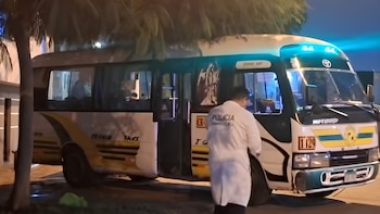 Un perito de la policía vestido con traje blanco inspecciona un minibús de transporte público estacionado de noche en una vía urbana
