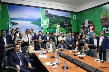 Un grupo de personas vestidas con camisa blanca posa en un escenario frente a una pantalla con el logotipo de la UNE y confeti en el suelo