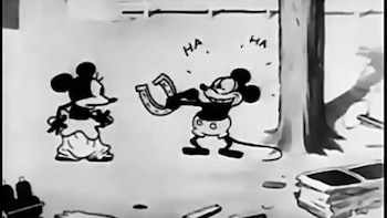 Caricatura en blanco y negro de Mickey Mouse riendo y sosteniendo una herradura, con Minnie Mouse de pie a la izquierda observándolo