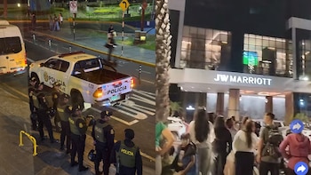 Composición con policías junto a un patrullero en una calle y personas reunidas de noche frente a la entrada del hotel JW Marriott