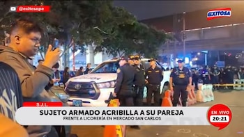 Vista nocturna de oficiales de policía y un Chevrolet SUV policial blanco en una calle, con civiles observando de fondo y un hombre tomando fotos