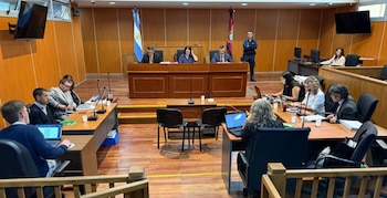 Una sala de audiencias judicial con un panel de tres jueces al fondo, un oficial de seguridad y varias mesas ocupadas por abogados con laptops