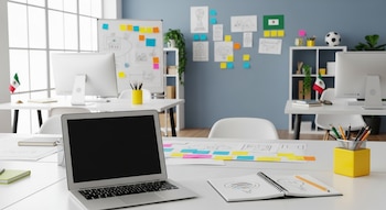 Oficina creativa vacía con escritorios blancos, laptops, libretas de bocetos y post-its de colores. Banderines de México y un balón de fútbol en estantes.