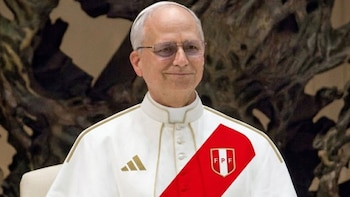 Primer plano de un hombre calvo con gafas, vestido con una túnica blanca que incorpora una franja roja diagonal y el escudo de la FPF