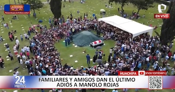Vista aérea de un funeral con una gran multitud de personas rodeando una tumba. Un féretro con la bandera peruana está bajo una carpa blanca en un cementerio