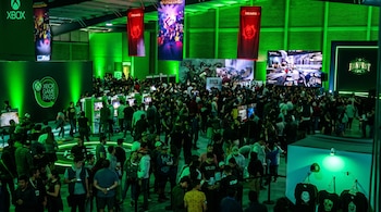 Multitud de personas en un recinto iluminado de verde entre pantallas de videojuegos y carteles de Xbox.