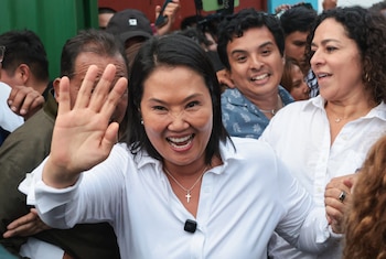Keiko Fujimori, vestida con una camisa blanca, sonríe y saluda con la mano derecha levantada, rodeada por varias personas