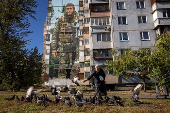 Una mujer alimenta palomas frente a un mural del artista callejero ucraniano Eugene Gladenko, que muestra al soldado ucraniano caído Maksym Bordus, en Kiev (REUTERS/Thomas Peter)