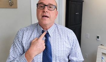 Hombre con gafas y camisa a cuadros que señala con su dedo índice el nudo de su corbata azul