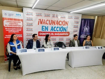Cinco personas sentadas en una mesa frente a un banner con el texto "¡VACUNACIÓN EN ACCIÓN! CONTRA EL SARAMPIÓN". Se aprecian logos de instituciones de salud