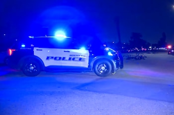 Una patrulla de policía con luces azules encendidas se encuentra detenida de noche en una calle junto a bicicletas tiradas sobre el asfalto