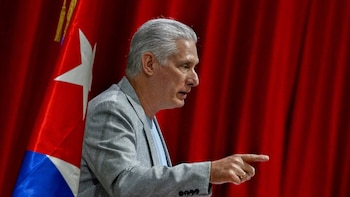 El Presidente de Cuba, de perfil, con cabello gris y blazer gris, señalando con el dedo derecho. Se ve la bandera cubana y cortinas rojas detrás