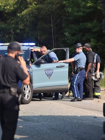 Varios agentes de la Policía Estatal de Massachusetts permanecen junto a un vehículo policial con la puerta abierta