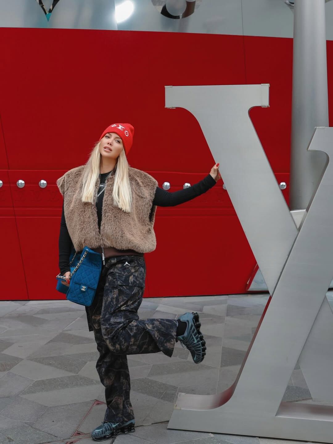 Cargo, chaleco de piel, remera negra y gorro de lana y cartera de Chanel para posar en la puerta de la tienda de Louis Vuitton