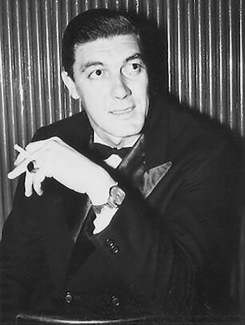 Retrato en blanco y negro de Alberto Morán, un hombre de cabello oscuro peinado hacia atrás, traje oscuro y pajarita, sosteniendo un cigarrillo