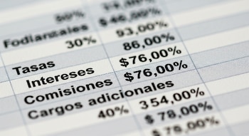 Un documento impreso muestra una tabla con las palabras Tasas, Intereses, Comisiones, Cargos adicionales, cifras monetarias y porcentajes.