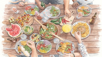 Ilustración acuarela de una vista aérea de amigos compartiendo una mesa de madera llena de ensaladas, frutas, brochetas, nachos y bebidas.