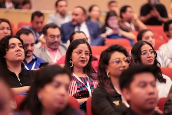 Tres personas hablan sentadas en sillones blancos en un escenario frente a una pantalla azul con la inscripción Guatemala AbreLatam ConDatos