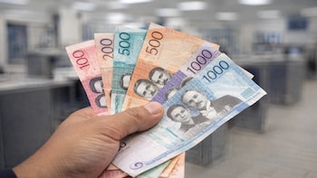 Circulación de pesos dominicanos: Mano exhibe billetes en entorno bancario - VisualesIA ScribNews