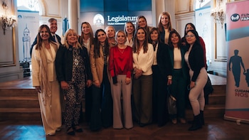 Grupo de personas, mayormente mujeres, sonriendo para una foto. Al fondo, un banner con el logo de la Legislatura de la Ciudad de Buenos Aires y otro de Funda Familias