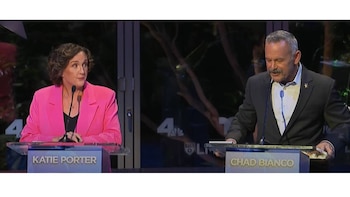 Katie Porter con un blazer rosa y Chad Bianco con traje oscuro y bigote, de pie en podios con micrófonos en un debate televisado