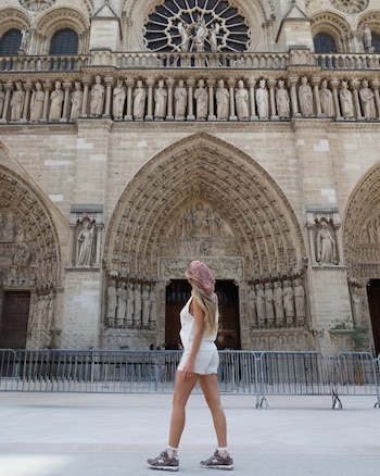 Mujer joven de espaldas con pañuelo y vestimenta blanca, de pie frente a la fachada de una catedral gótica con esculturas y un rosetón