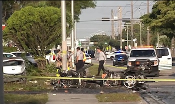 Coche destrozado y SUV blanco dañado en calle. Vehículos de emergencia y personal policial y de rescate en la escena, con cinta de seguridad amarilla