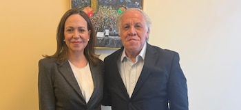 María Corina Machado, con blazer gris, y Luis Almagro, con traje oscuro, de pie y sonriendo, con un cuadro colorido de fondo