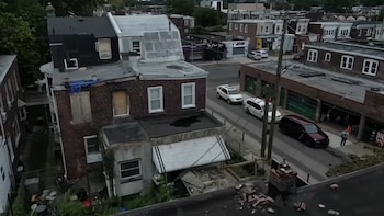 Vista aérea de un edificio de ladrillo rojo con ventanas tapiadas junto a una calle con automóviles estacionados en Filadelfia