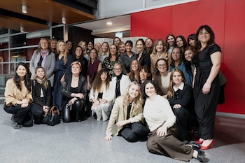 Un grupo de varias mujeres posa frente a un cartel con la inscripción Women in Compliance y una pared roja al fondo