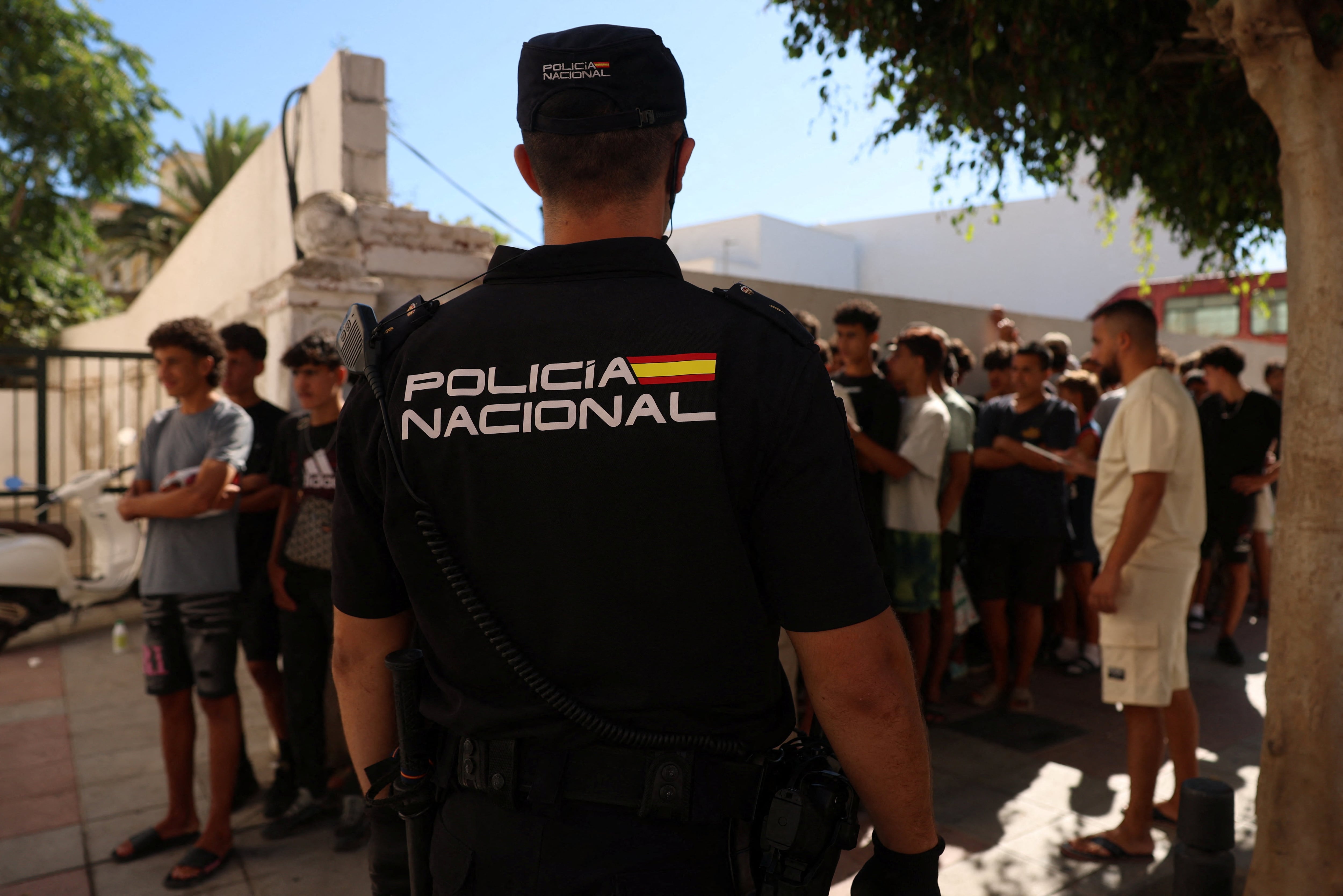 Un agente de policía monta guardia mientras niños migrantes hacen cola frente a una comisaría para ser registrados tras los cruces masivos de migrantes a pie y por mar desde Marruecos hacia territorio español, en Ceuta, España. 6 de agosto de 2026. REUTERS/Violeta Santos Moura