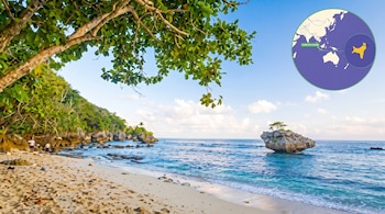 Una playa tropical con arena, mar azul, acantilados verdes, rocas, dos personas, un árbol frondoso y un mapa circular de la Isla de Navidad.