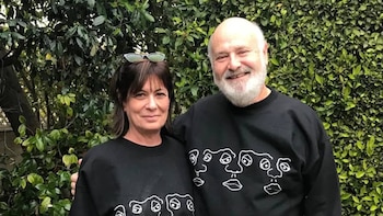 Nick Reiner, hombre calvo con barba, y Michele Singer Reiner, mujer de cabello oscuro, sonríen con sudaderas negras frente a hojas verdes