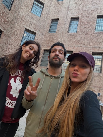 Autofoto de tres personas frente a una pared alta de ladrillos vistos con ventanas de marco oscuro