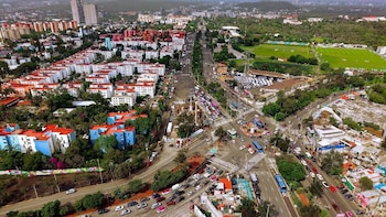 Vista aérea de una intersección urbana con vehículos, edificios de departamentos, zonas arboladas y una obra en el camellón
