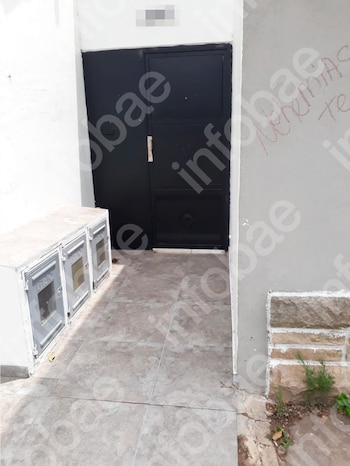 Fachada exterior con una puerta doble de metal negra. A la izquierda, tres cajas de servicios públicos blancas. El suelo es de baldosas
