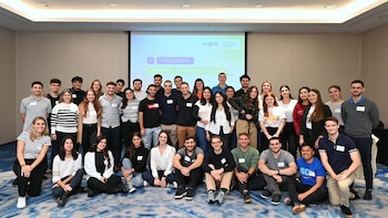 Un grupo grande de jóvenes adultos sonríe para una foto en un evento; una pantalla al fondo muestra 'Programa Jóvenes Profesionales' y logos de energía