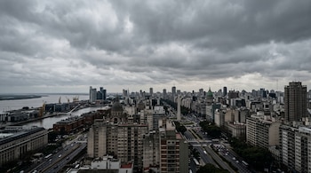 Vista aérea de la ciudad de Buenos Aires con edificios, avenidas, el Obelisco y el río bajo nubes grises.