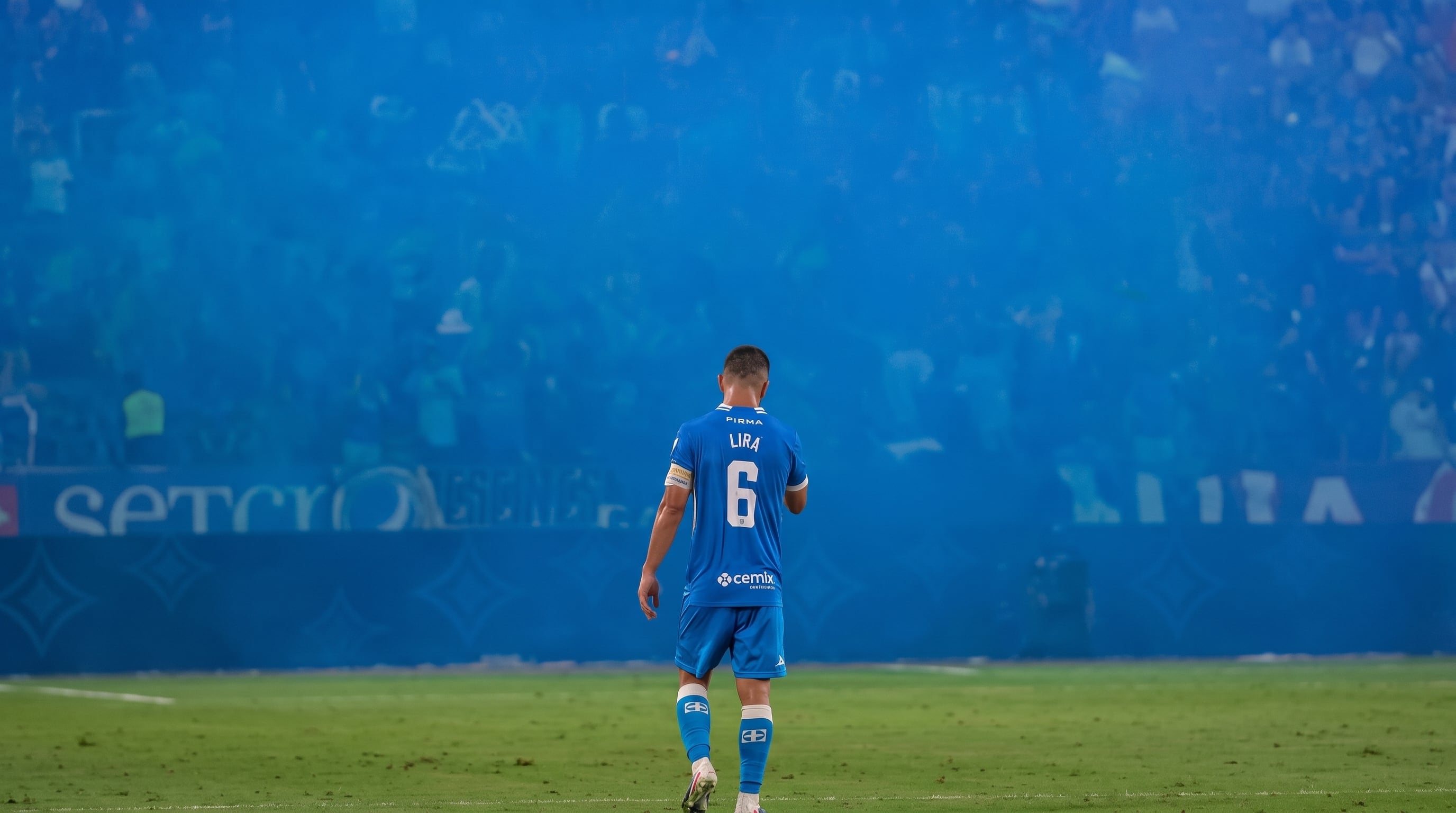 El futbolista Erik Lira camina de espaldas por la cancha mientras el humo azul cubre la grada del estadio. (Imagen Ilustrativa Infobae)