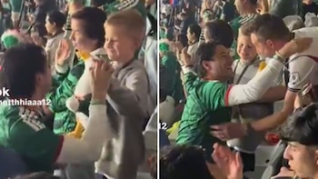Dos hombres, un niño y un peluche blanco. Un hombre con camiseta verde da un peluche blanco a un niño. Otro hombre con camiseta verde abraza a un hombre con camiseta blanca