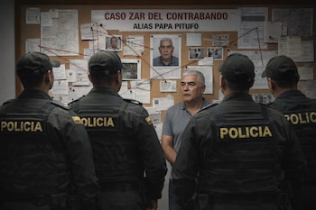 Hombre canoso, Alias Papa Pitufo, de pie frente a cuatro policías de espaldas, ante un tablero de corcho con mapas y documentos de investigación.