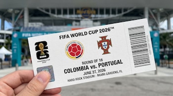 Una mano sostiene un tiquete de la Copa Mundial de la FIFA 2026 para el partido Colombia vs. Portugal, con el Hard Rock Stadium de Miami borroso al fondo.