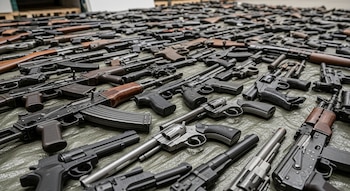 Pistolas, revólveres, fusiles y otras armas de fuego de distintos calibres y modelos, todas dispuestas sobre una lona verde.