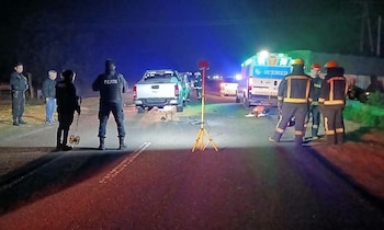 Vista nocturna de una carretera con agentes de policía, personas, una camioneta, una ambulancia y un trípode de luz amarilla